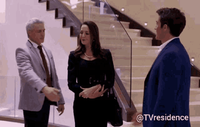 a man in a suit and tie talks to a woman in a black dress and a man in a blue suit and tie
