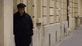 a man wearing a flat cap and a black coat is standing on a sidewalk