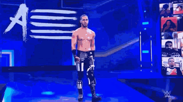 a shirtless wrestler is standing on a stage in front of a sign that says a