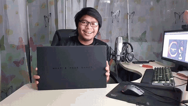 a man holding up a laptop that says what is your game