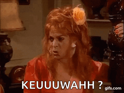 a woman with red hair and a flower in her hair is sitting on a couch and says keuuuwahh ?