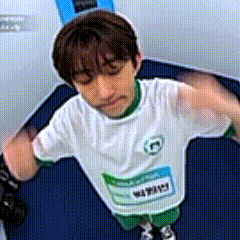 a young boy wearing a white shirt and green shorts is standing on a blue carpet .