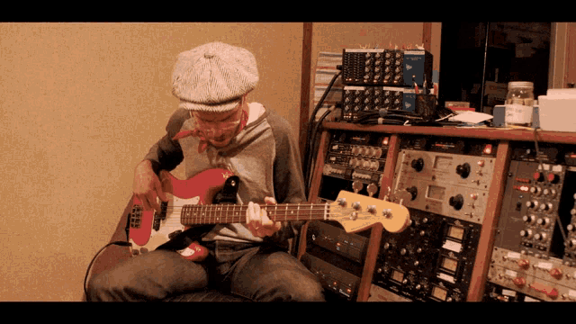 a man is playing a red guitar in front of a bunch of electronic equipment