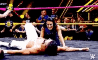 a man is laying on the ground in a wrestling ring while a woman looks on .