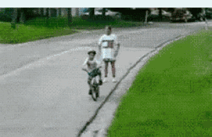 a boy is riding a bike down a street while a woman watches .