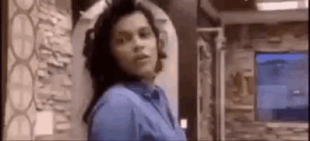 a woman in a blue shirt is standing in a room in front of a tv .