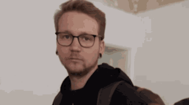 a man wearing glasses and a backpack is standing in a room with a woman .