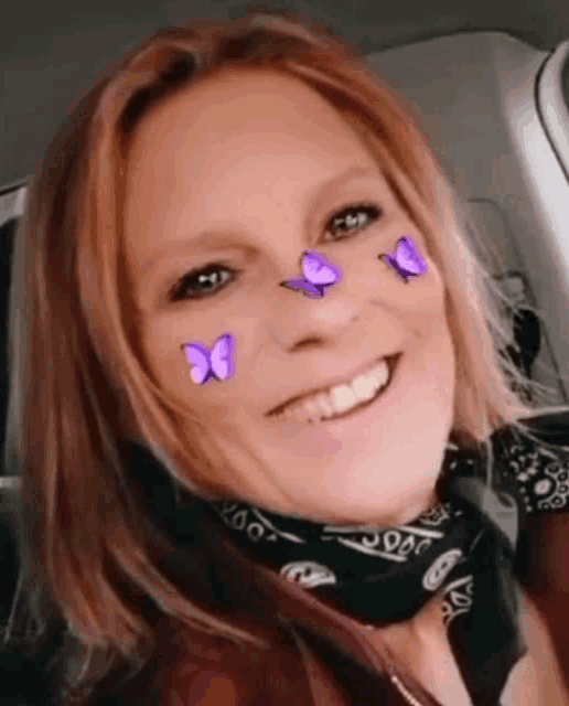 a woman wearing a bandana and purple butterflies on her face is smiling .