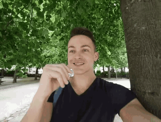 a man is taking a selfie while leaning against a tree in a park .