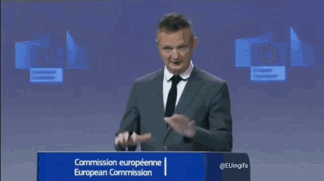 a man in a suit and tie stands at a podium that says commission european commission