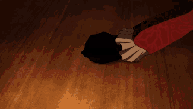 a person 's hand is reaching for a small black object on a wooden floor