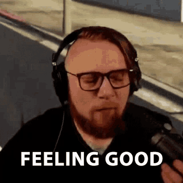 a man with a beard wearing headphones and glasses is talking into a microphone and saying `` feeling good '' .