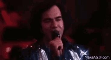 a man is singing into a microphone while wearing a sequined jacket .