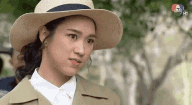 a woman wearing a hat and a white shirt is standing in front of a tree .