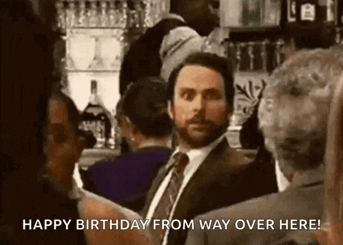 a man in a suit and tie is standing in a crowd and says happy birthday from way over here .