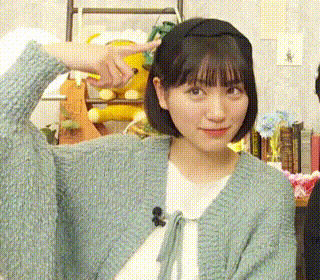 a young woman wearing a headband and a green cardigan is pointing at something .