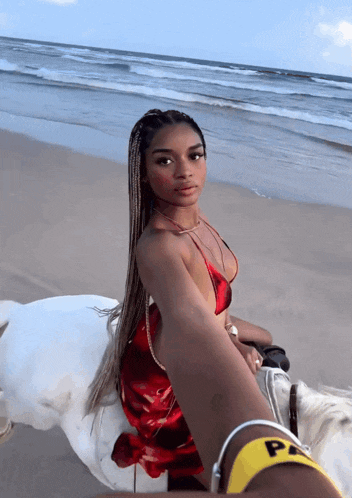 a woman in a red dress is riding a horse on the beach