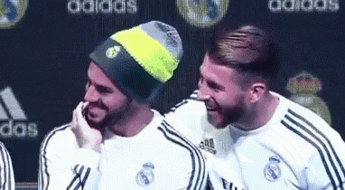 a couple of men are standing next to each other and laughing . one of the men is wearing a beanie .