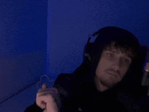 a man wearing headphones and a hoodie is sitting in a dark room .
