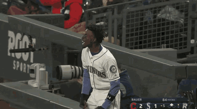 a man in a mariner jersey stands in the dugout