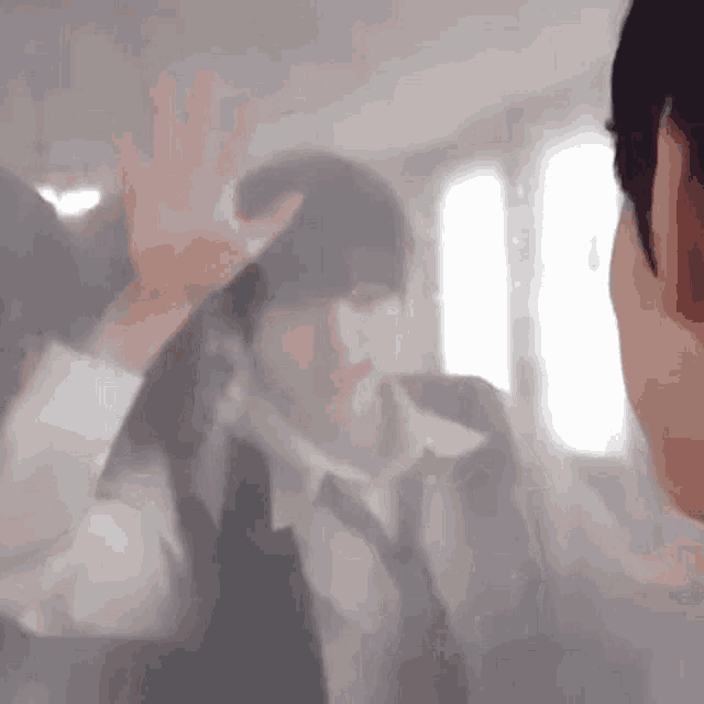 a man in a suit and tie is waving his hand at another man in a room .