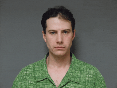 a man in a green shirt looks at the camera with a serious look on his face