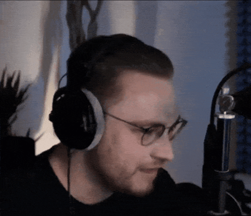 a man wearing headphones and glasses is sitting in front of a microphone .