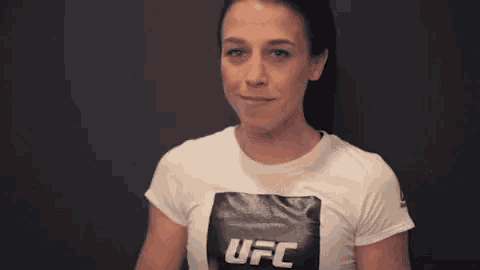 a woman wearing a white ufc t-shirt is smiling and giving a high five .