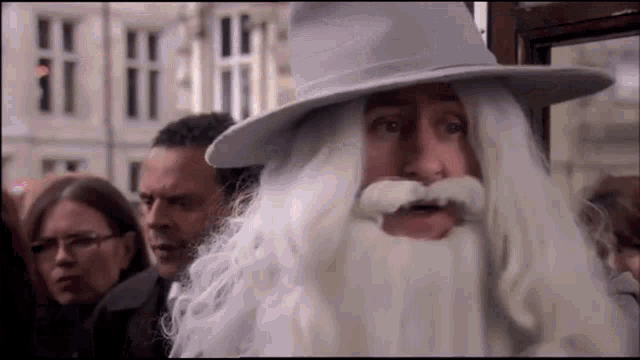 a man wearing a white hat and beard is standing in a crowd .