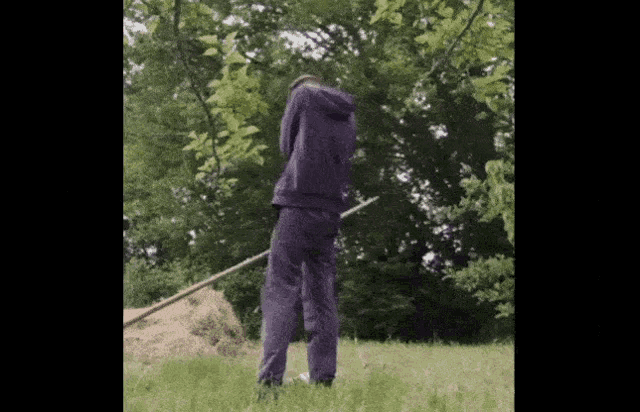 a man in a purple hoodie is standing in a field with a rake