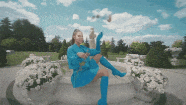 a woman in a blue dress is sitting on a fountain