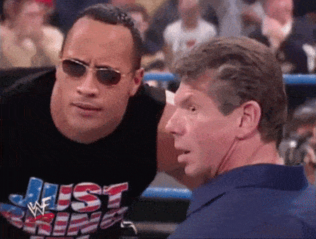 a man wearing a shirt that says " just chill " talks to another man in a wrestling ring