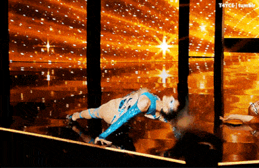 a woman in a blue bodysuit is doing a handstand in front of a gold background