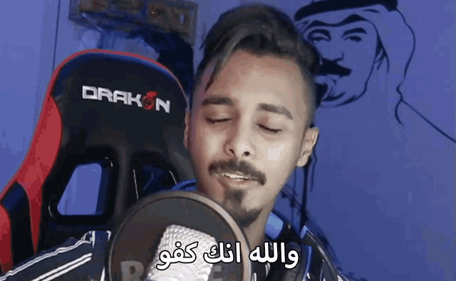 a man is singing into a microphone with a drakon chair in the background
