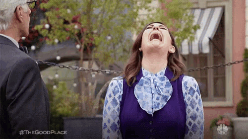 a woman is laughing while standing in front of a man in a suit .