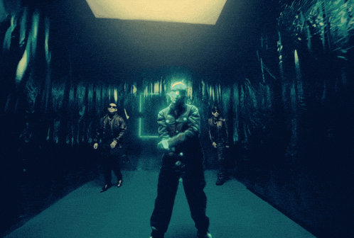 a group of men are standing in a dark room with a light above them