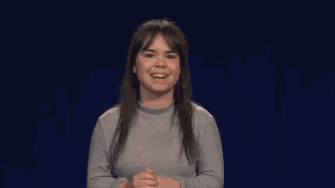 a woman in a grey sweater is making a devil horns sign with her hands