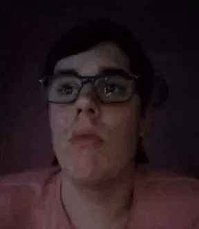 a person wearing glasses and a pink shirt is making a funny face with their mouth open .