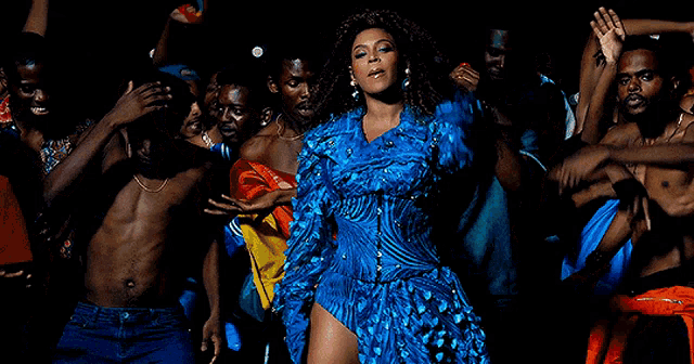 a woman in a blue dress is surrounded by a group of men dancing .
