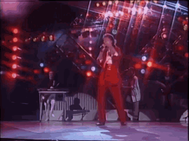 a man in a red suit is singing into a microphone on stage .
