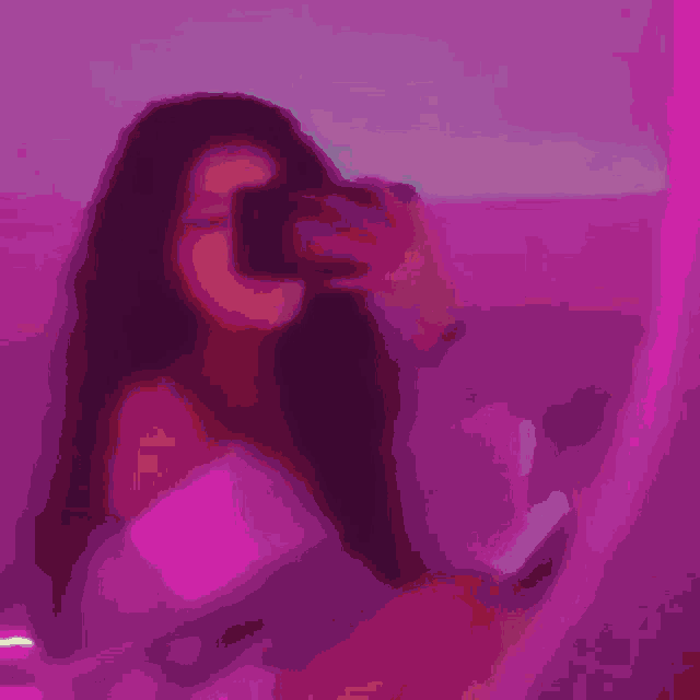 a woman is taking a picture of herself in a mirror with a pink light behind her