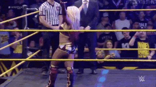 a woman is standing in a wrestling ring while a referee watches .