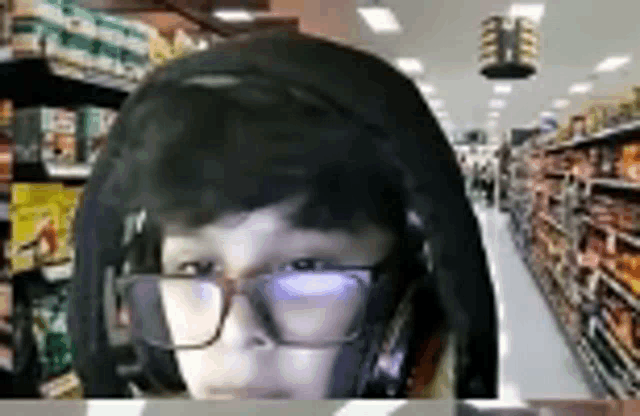 a man wearing glasses and headphones is standing in front of a grocery store aisle .