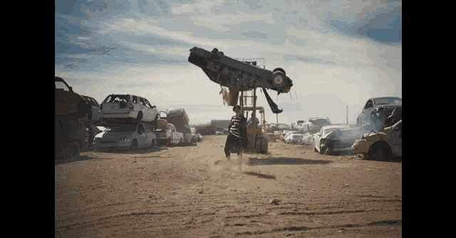 a man is lifting a car on a forklift in a scrap yard .