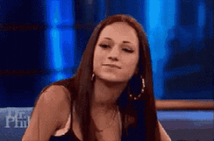 a woman with long hair and hoop earrings is sitting in front of a blue wall .