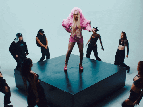 a woman in a pink wig stands on a stage surrounded by other dancers