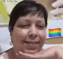 a woman is smiling and holding her hand to her chin in front of a rainbow flag .