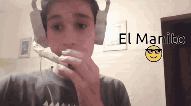 a boy wearing headphones is eating a candy bar and the words el manito are visible