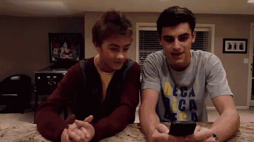 two young men looking at a cell phone one of whom is wearing a deca shirt