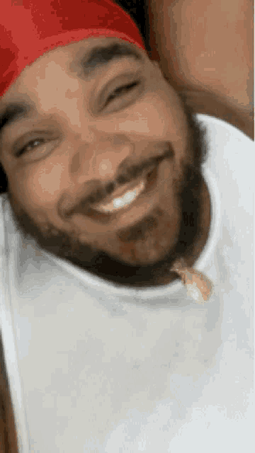 a man with a beard wearing a red headband and a white tank top is smiling .